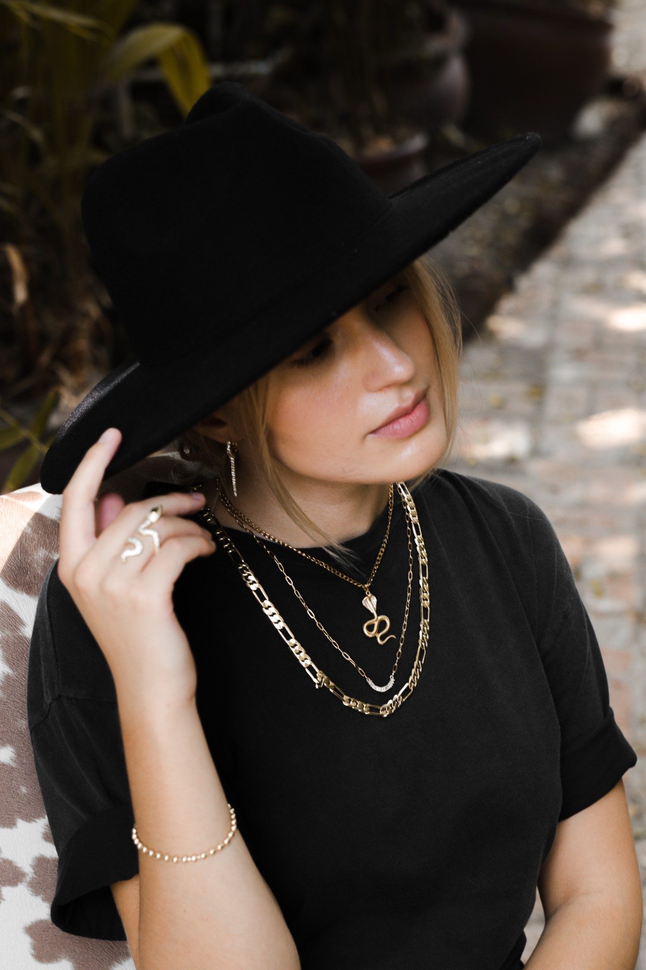 Model in a black hat and tee wearing layered gold chains and a snake ring