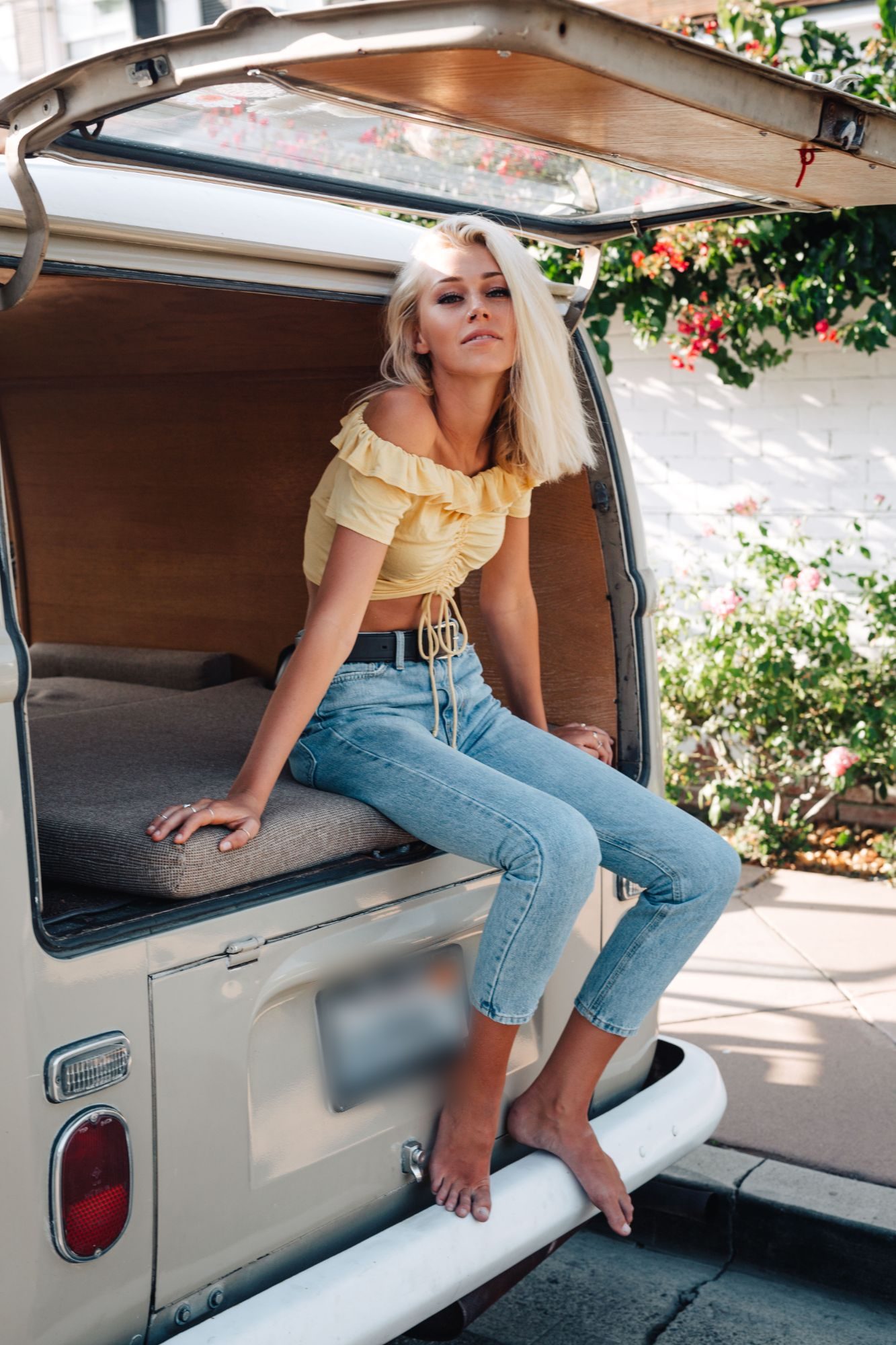 Model in a yellow ruffle crop top and jeans sitting in the back of a vintage VW bus