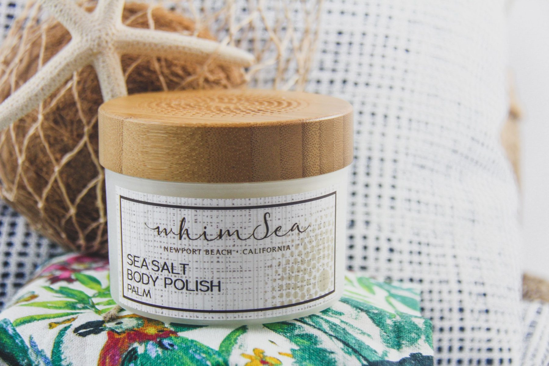 WhimSea Sea Salt Body Polish jar with a starfish and coconut on woven textiles